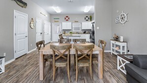 A modern kitchen with white cabinets, a central island, and a dining area with wooden chairs. - Walk to Beach~Heated Pool~BBQ Area~Balcony~Island (Corpus Christi)