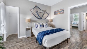 A bedroom with a bed, nightstands, a ceiling fan, and a wall-mounted decorative piece. - Walk to Beach~Heated Pool~BBQ Area~Balcony~Island (Corpus Christi)