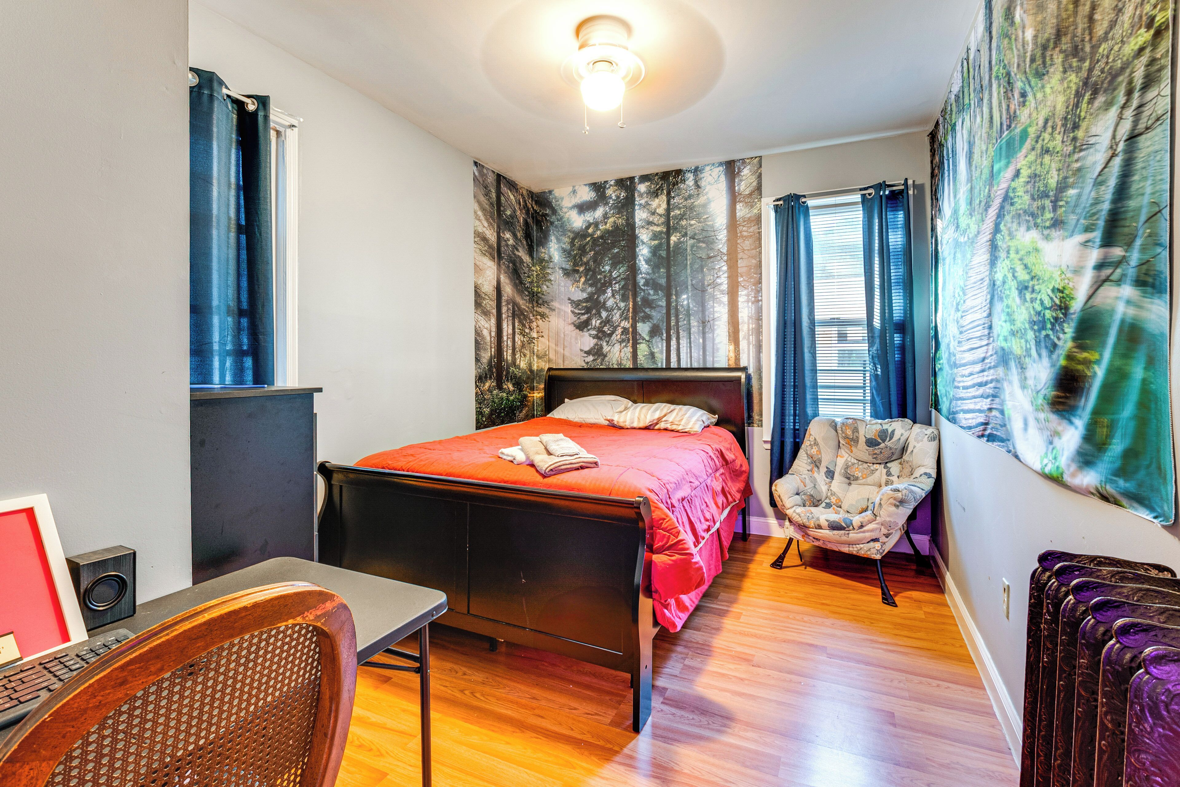 A bedroom with a bed, a chair, a desk, and a large forest-themed wall tapestry.