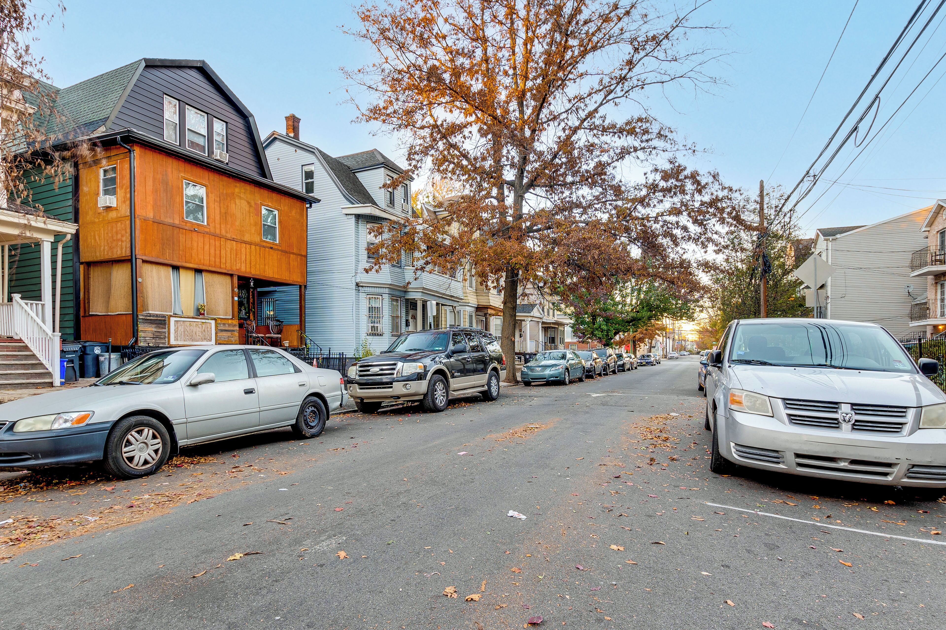 Een woonstraat met huizen, geparkeerde auto's en herfstbladeren op de grond.