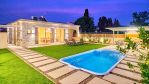 A backyard with a swimming pool, a stone house, and a covered patio area. - Villa Cinque Elementi by Estia (Ionian Islands)