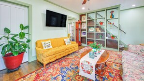 A living room with a yellow sofa, a coffee table, a red potted plant, a patterned rug, and a bookshelf with various items. - 18 Mi to Skiing: Colorful Home in Springfield! (Springfield)
