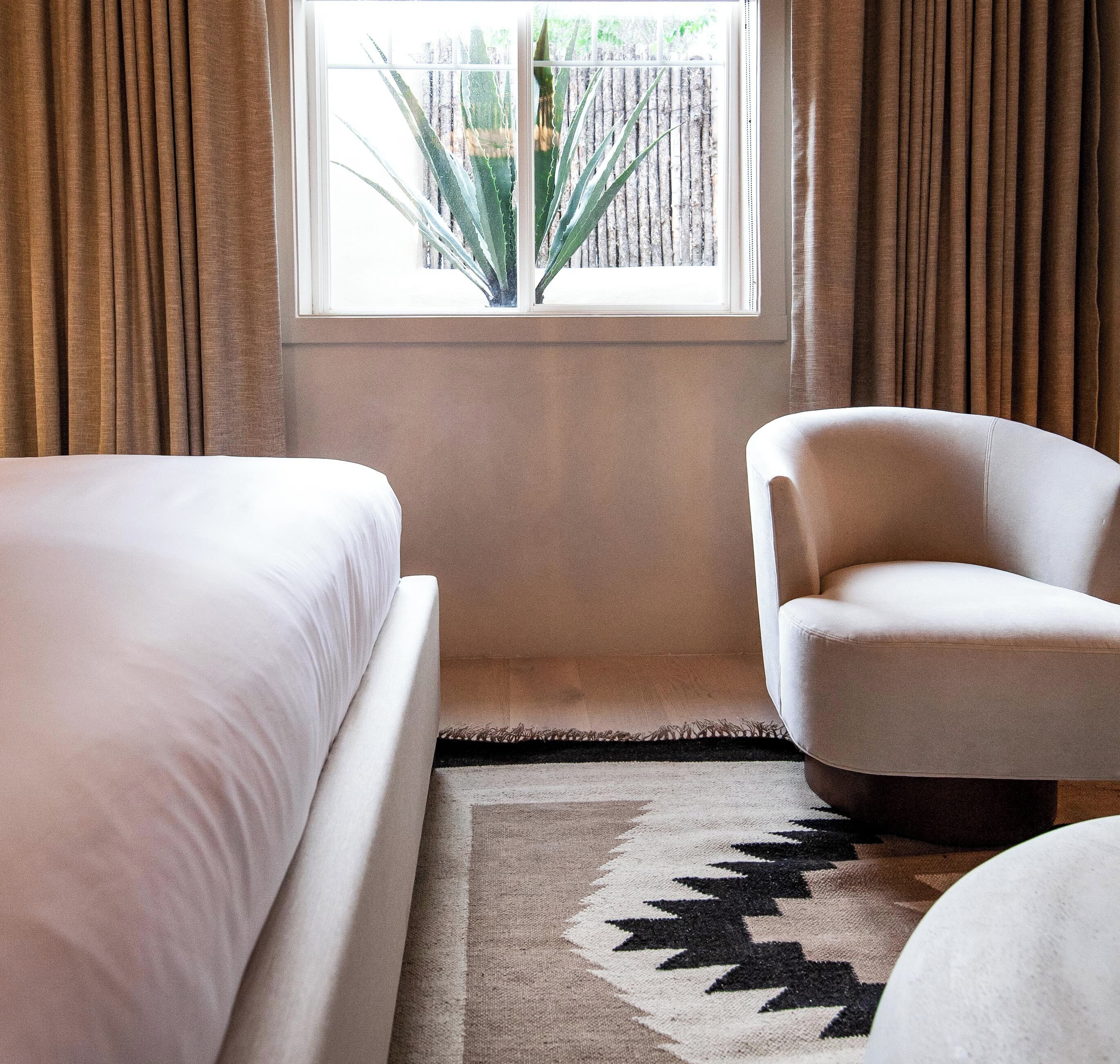 Une chambre avec deux lits, une chaise, une fenêtre avec des rideaux et un tapis à motifs.
