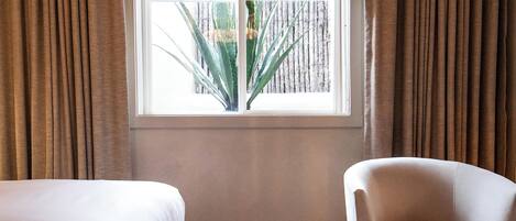 Une chambre avec deux lits, une chaise, une fenêtre avec des rideaux et un tapis à motifs.