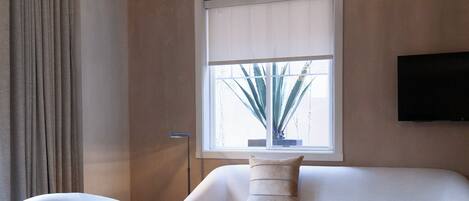 A modern living room with a white sofa, a white armchair, and a white coffee table. There is a large window with a view of a plant outside.
