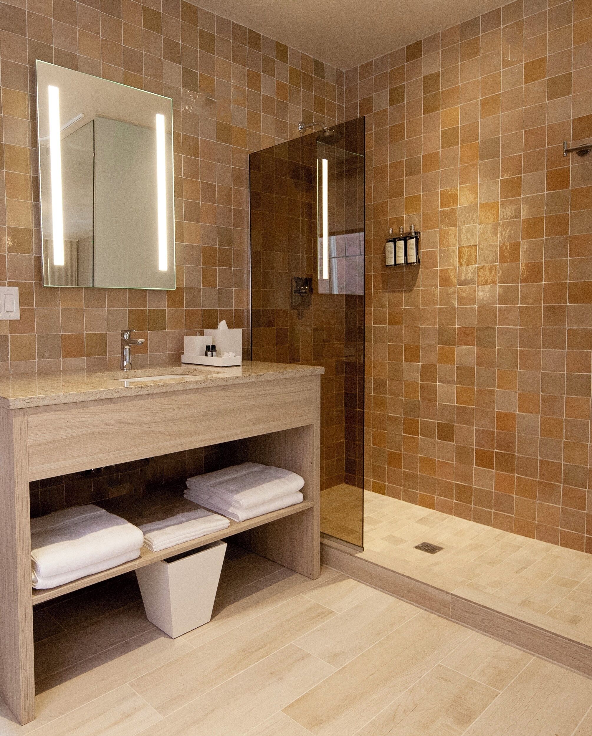 Un baño moderno con tocador de madera, cabina de ducha de vidrio y salpicadero de azulejos.