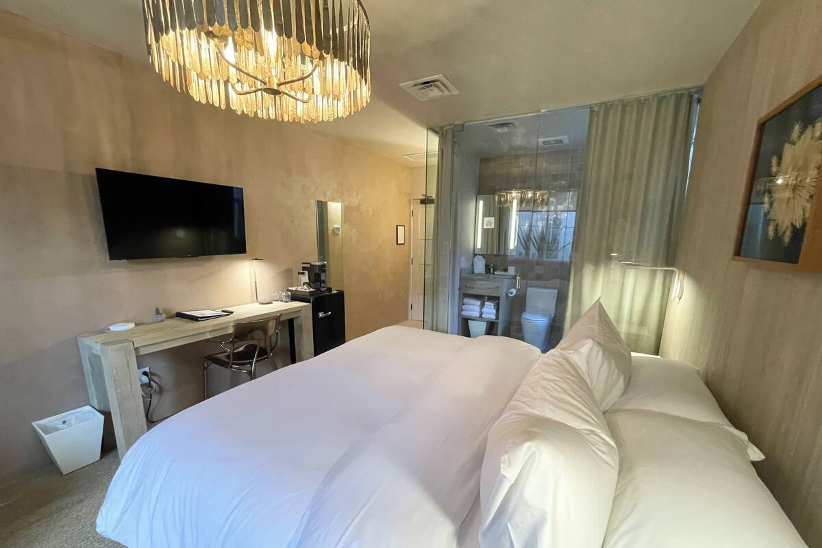 Une chambre d’hôtel dotée d’un grand lit, d’un bureau avec une chaise, d’un téléviseur fixé au mur et d’une salle de bain visible à travers une paroi en verre.