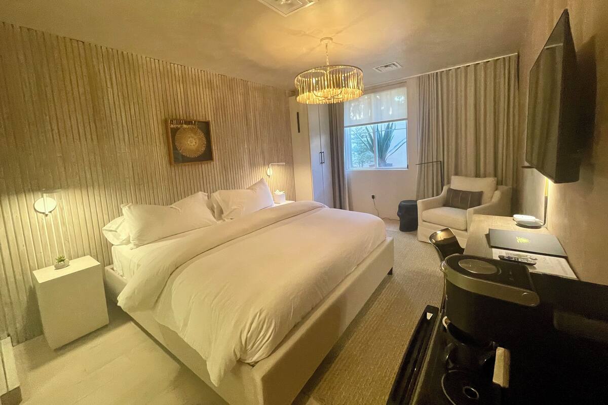 Une chambre d’hôtel avec un grand lit, un bureau avec un ordinateur portable, une chaise, une télévision et une fenêtre avec des rideaux.