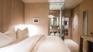 A modern bedroom with a large bed, a bedside table, a mirror, and a bathroom visible through a glass door. - Palace Modern Hotel at the Plaza (Santa Fe)