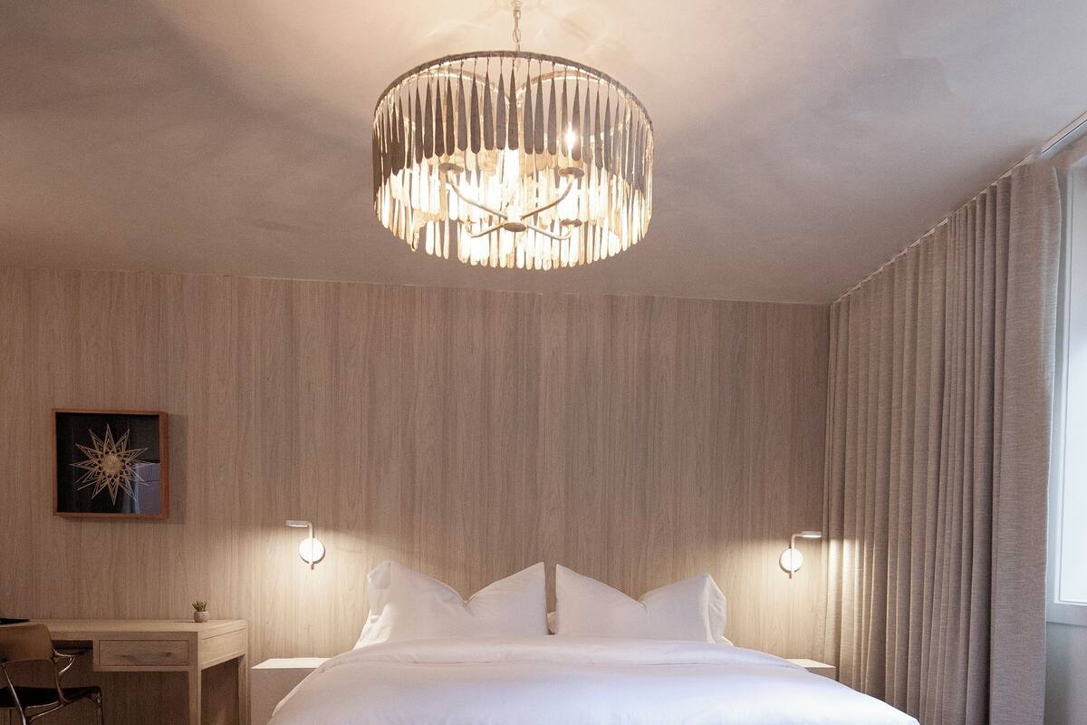 Une chambre d’hôtel moderne avec un grand lit, un bureau et une table ronde agrémentée d’une plante.
