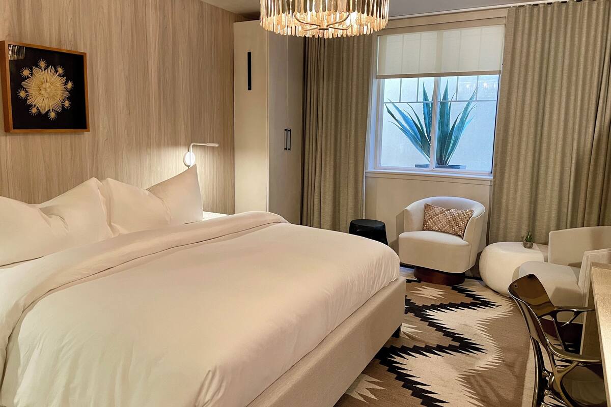 Une chambre d’hôtel moderne dotée d’un grand lit, d’un coin salon avec un fauteuil, une petite table et une fenêtre avec des rideaux.