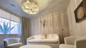 A modern living room with a beige sofa, two armchairs, a round ottoman, a chandelier, and a framed artwork on the wall. - Palace Modern Hotel at the Plaza (Santa Fe)