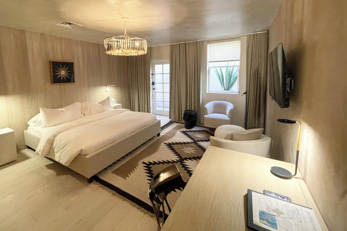 Une chambre d’hôtel avec un grand lit, un bureau, une chaise, une télévision et une fenêtre avec des rideaux.
