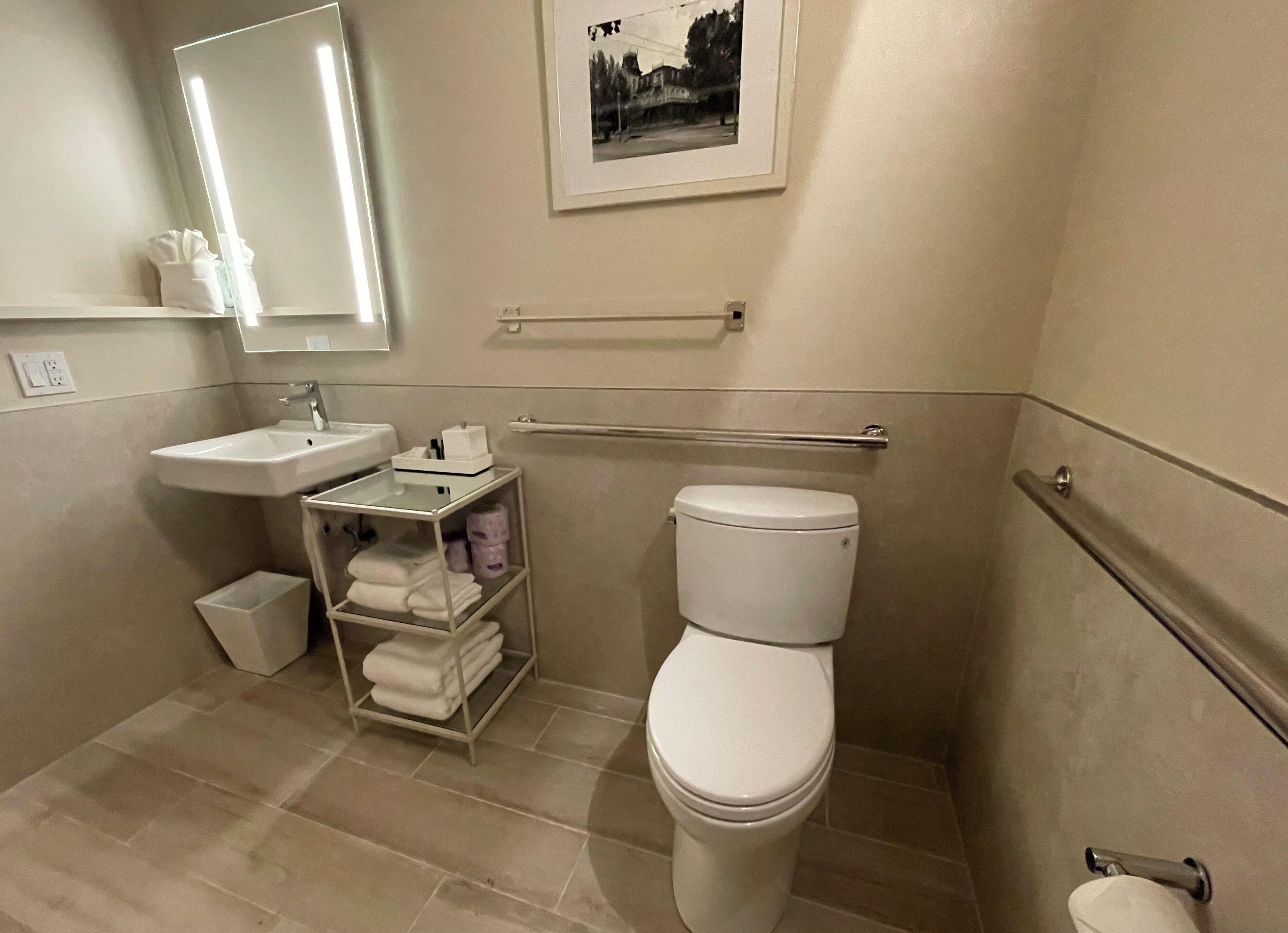 Un bagno con un lavandino bianco, un water, un portasciugamani e un quadro appeso al muro.