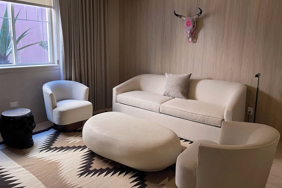Un salon moderne avec un canapé, des fauteuils, un tapis à motifs, un élément décoratif en forme de crâne accroché au mur et un luminaire suspendu.