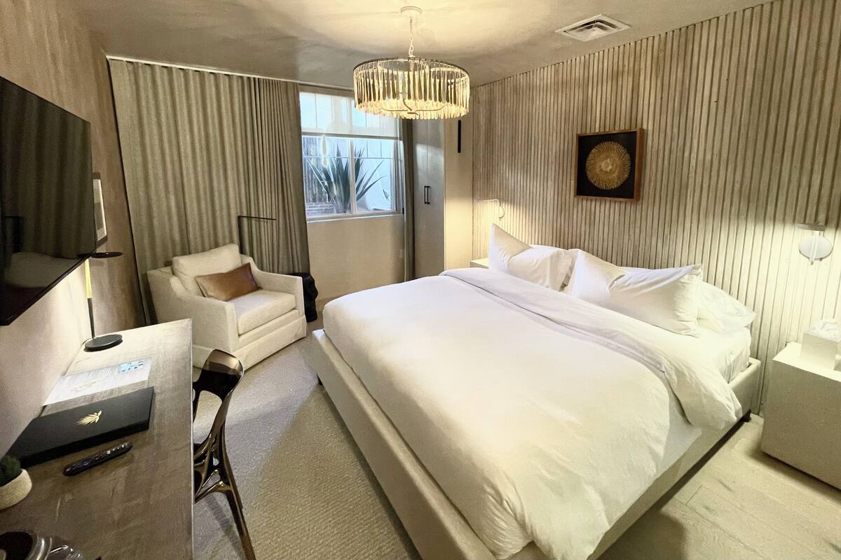 Une chambre d’hôtel avec un grand lit, une chaise, un bureau avec un ordinateur portable, une lampe et une fenêtre avec des rideaux.