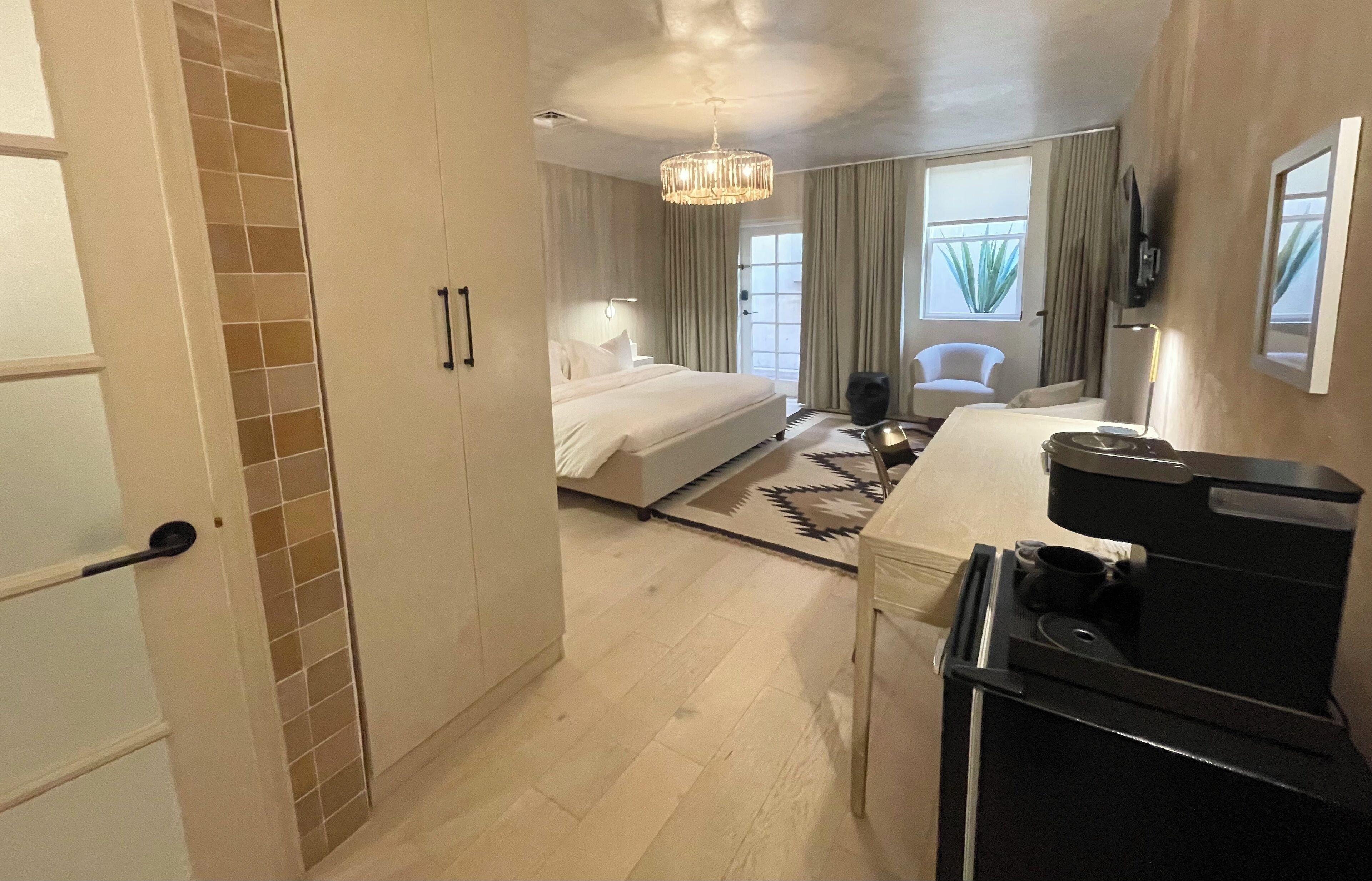 Ein Hotelzimmer mit einem Bett, einem Schreibtisch mit Kaffeemaschine, einem Fernseher und einem Fenster mit Vorhängen.
