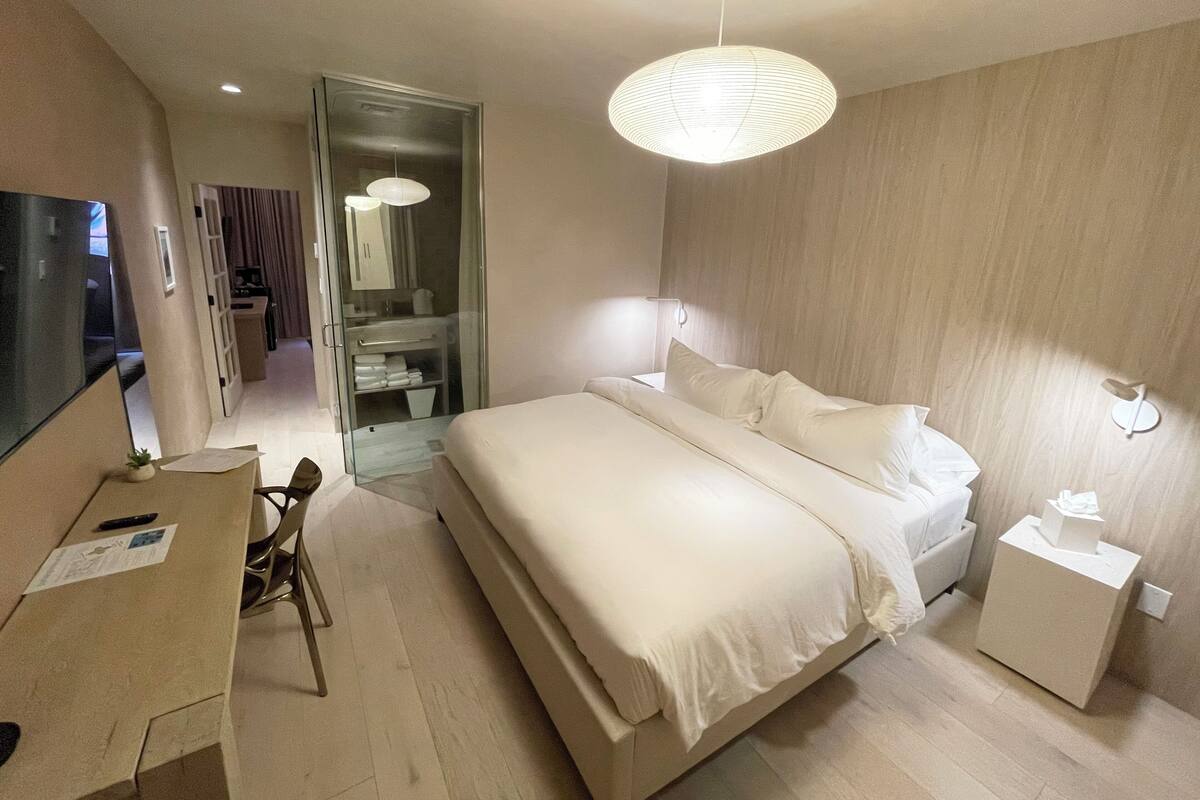 Une chambre d’hôtel moderne avec un grand lit, un bureau avec une chaise, une petite table de chevet et une armoire.