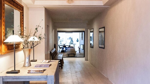 A hallway with a chandelier, a table with books and a vase of flowers, and a view into another room with a table and chairs. - Palace Modern Hotel at the Plaza (Santa Fe)