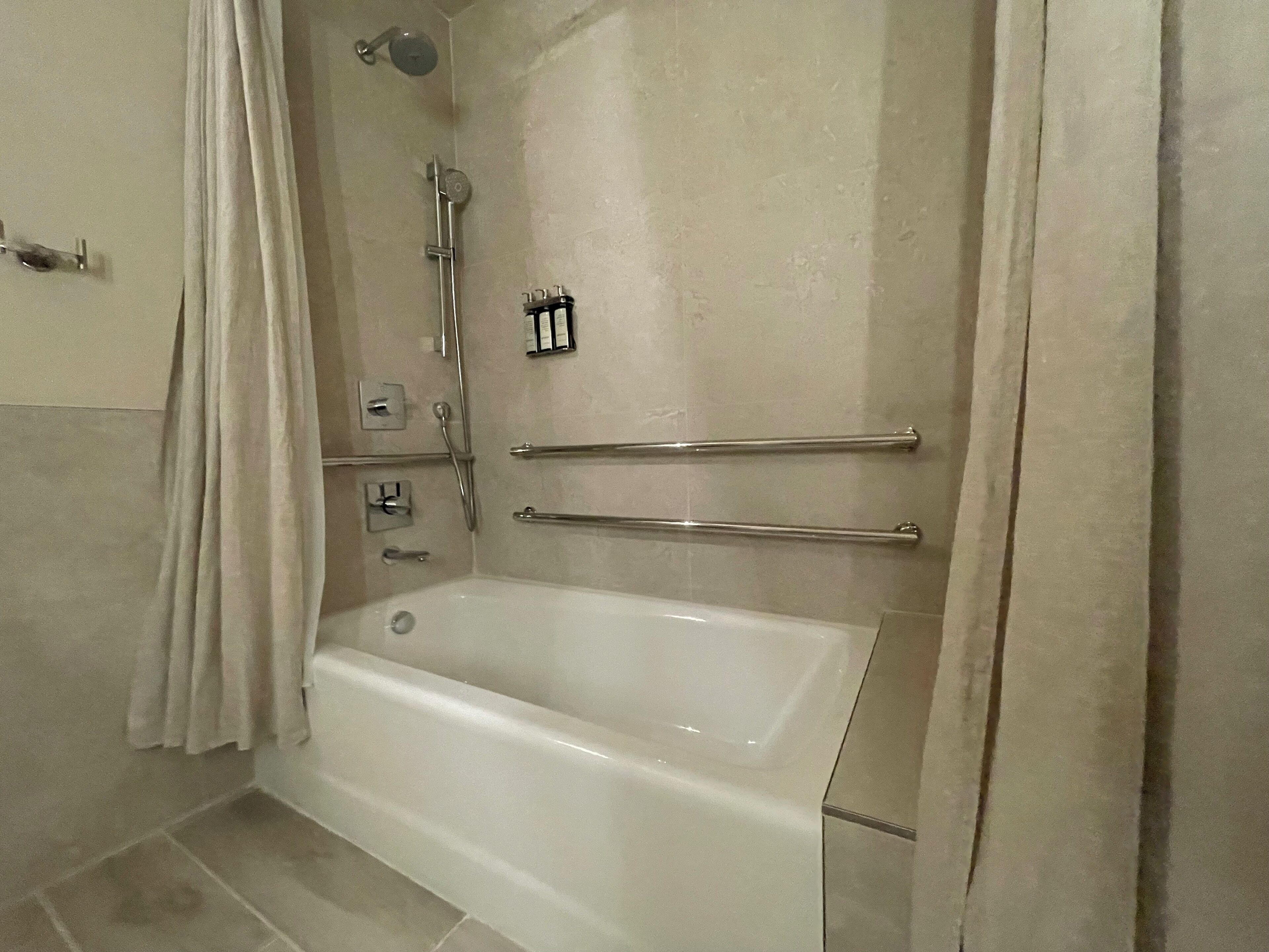 Un baño con bañera, barras de apoyo, cabezal de ducha y un perchero para toallas.