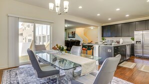 A modern kitchen with dark cabinets, a stainless steel refrigerator, and a dining area with a glass table and grey chairs. - Centrally Located Home in Fredericksburg! (Fredericksburg)