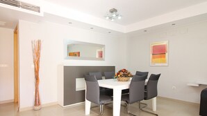 Ein moderner Essbereich mit einem weißen Tisch, grauen Stühlen, einem Blumenstrauß, einem Spiegel über dem Tisch und einem Gemälde an der Wand.
