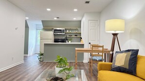 A modern kitchen with a microwave, stove, and refrigerator. There is a dining area with a yellow sofa and a lamp. - Spacious Entire Home in Great Location ! (Chamblee)