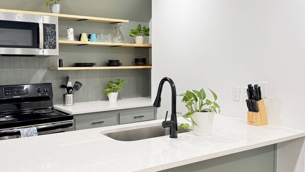 A modern kitchen with a built-in microwave, stove, and sink. There are shelves with glassware and plants, and a knife block on the countertop. - Spacious Entire Home in Great Location ! (Chamblee)