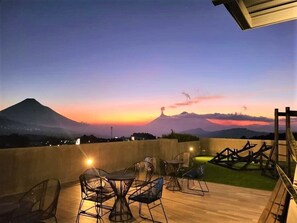 A terrace with outdoor seating and a view of a mountain at sunset.