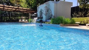 Una piscina con una cascada, rodeada por una pérgola y una estructura de piedra con diseño de jirafa.
