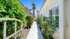 A narrow pathway flanked by lush greenery and a row of white buildings with large windows. - Charming 1-bedroom Casita in gated Duna La Quinta. Walk to Old Town & LQ Resort (La Quinta)