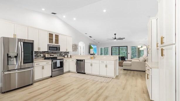 Une cuisine moderne avec des meubles blancs, des appareils en acier inoxydable et un plancher en bois.