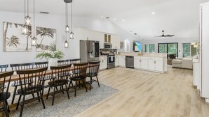 Une cuisine spacieuse équipée d’appareils modernes, un coin repas avec des chaises en bois et un ventilateur de plafond.