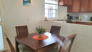 A dining area with a wooden table, four chairs, a potted plant, and a painting on the wall.