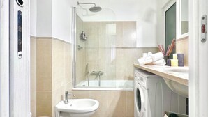 A modern bathroom with a glass-enclosed shower, a bidet, a washing machine, and a sink.