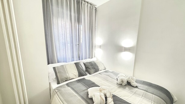 A neatly made bed with a striped bedspread and two pillows, a window with curtains, and wall-mounted lights.