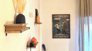 A room with a wall-mounted shelf holding books, a vase, and a guitar. There's a poster on the wall with a message.