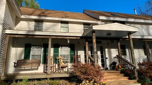 A two-story house with a porch, wooden chairs, and a bench. - UU Rowe Camp and Conference Center (Rowe)