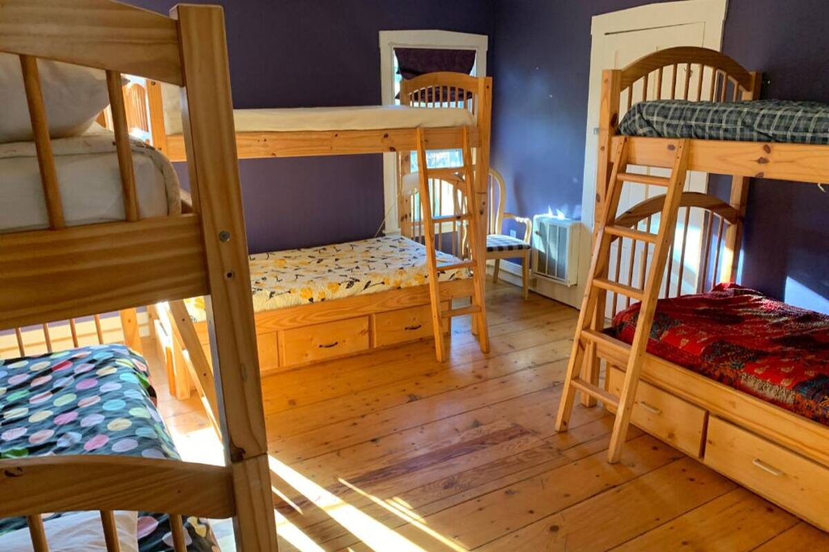 A bunk bed room with a desk and chair, wooden floors, and a window.