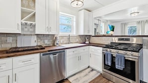 A modern kitchen with white cabinets, a stainless steel dishwasher, a built-in oven, and a wooden countertop.