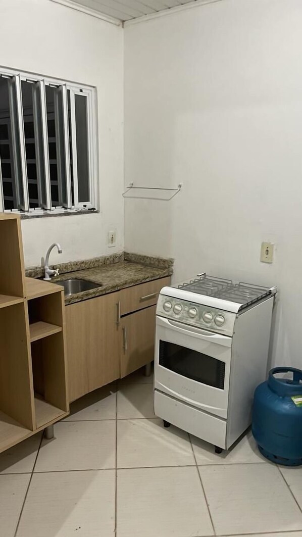 A compact kitchen with a gas stove, a sink, and a window with blinds.