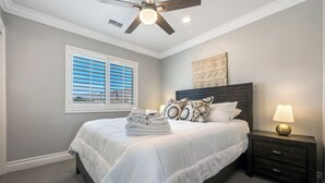 A bedroom with a bed, a nightstand, a lamp, a ceiling fan, and a window with blinds.
