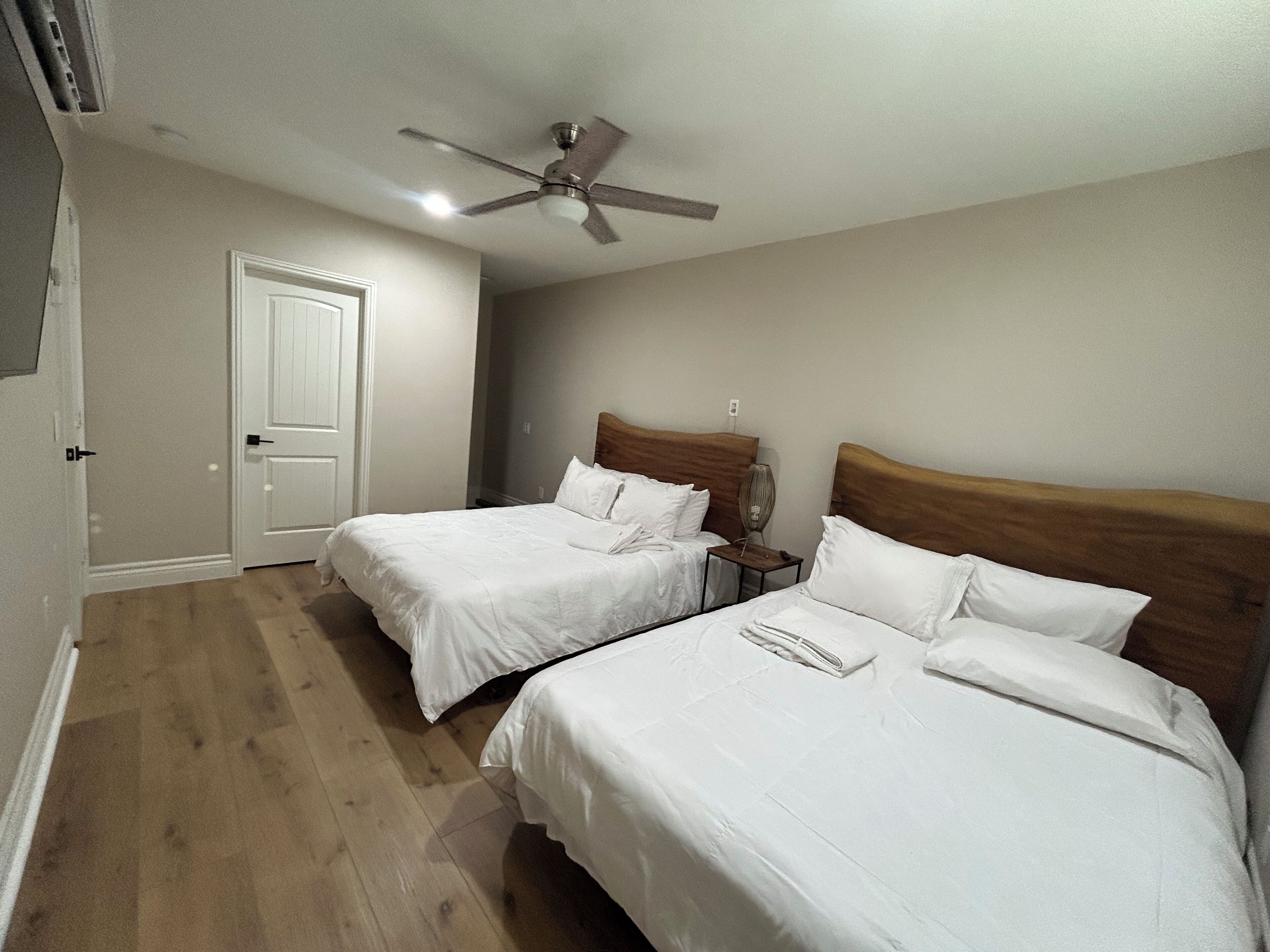 A bedroom with two single beds, a ceiling fan, a bedside table with a lamp, and a door.