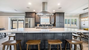 A modern kitchen with a large island, dark cabinetry, stainless steel appliances, and a bar area with stools.