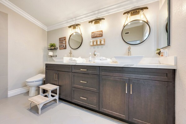 A modern bathroom with dark wood cabinets, a white sink, and two round mirrors with light fixtures.