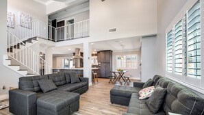 A spacious living area with a large sectional sofa, a dining table, and a staircase leading to an upper level.