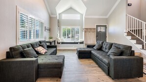 A spacious living room with two dark grey sofas, a wooden floor, and a staircase leading to an upper level.