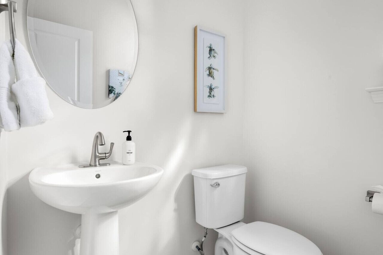 Un baño con un lavamanos blanco, un inodoro y un espejo. Hay un cuadro en la pared.