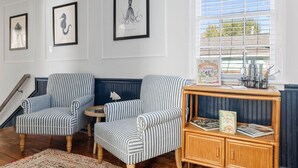 A room with striped armchairs, a small round table, a wooden side table with books, and framed artwork on the wall.
