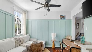 A cozy living room with a white sofa, a dining table, and a ceiling fan.